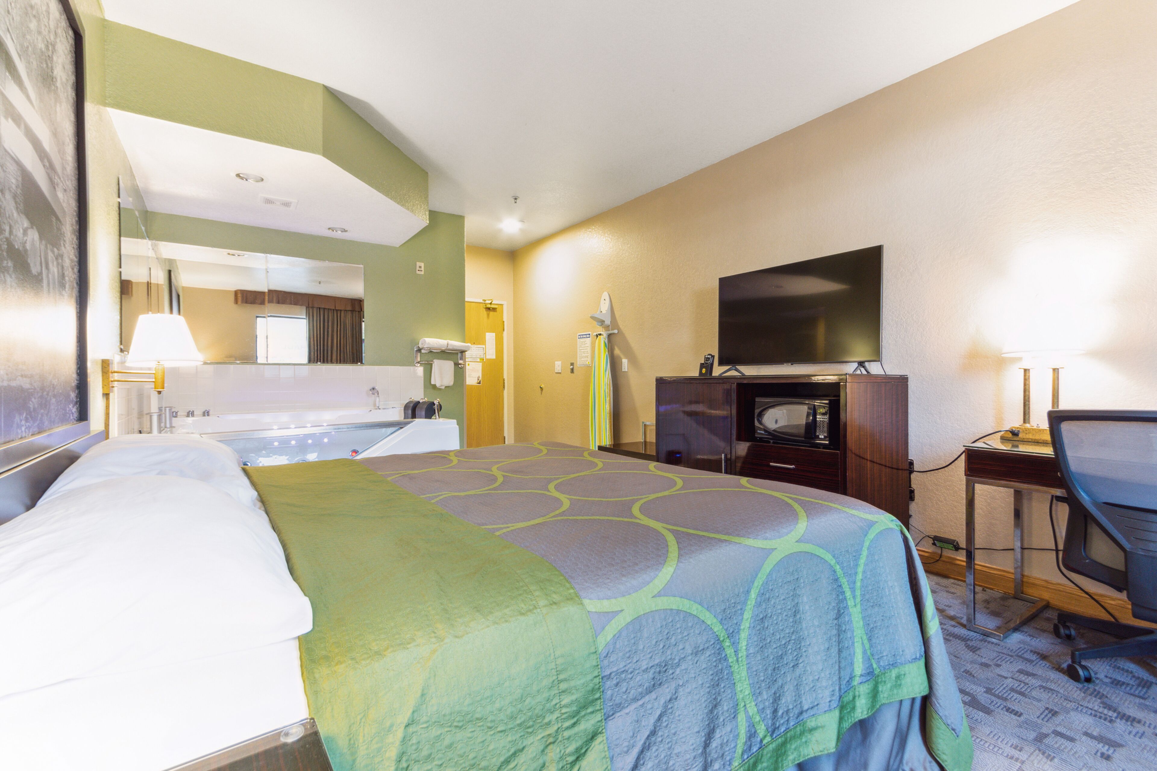 A hotel room with a bed, a desk with a chair, a television, and a bathroom with a bathtub and toilet.