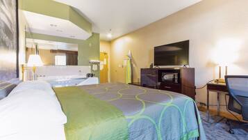 A hotel room with a bed, a desk with a chair, a television, and a bathroom with a bathtub and toilet.