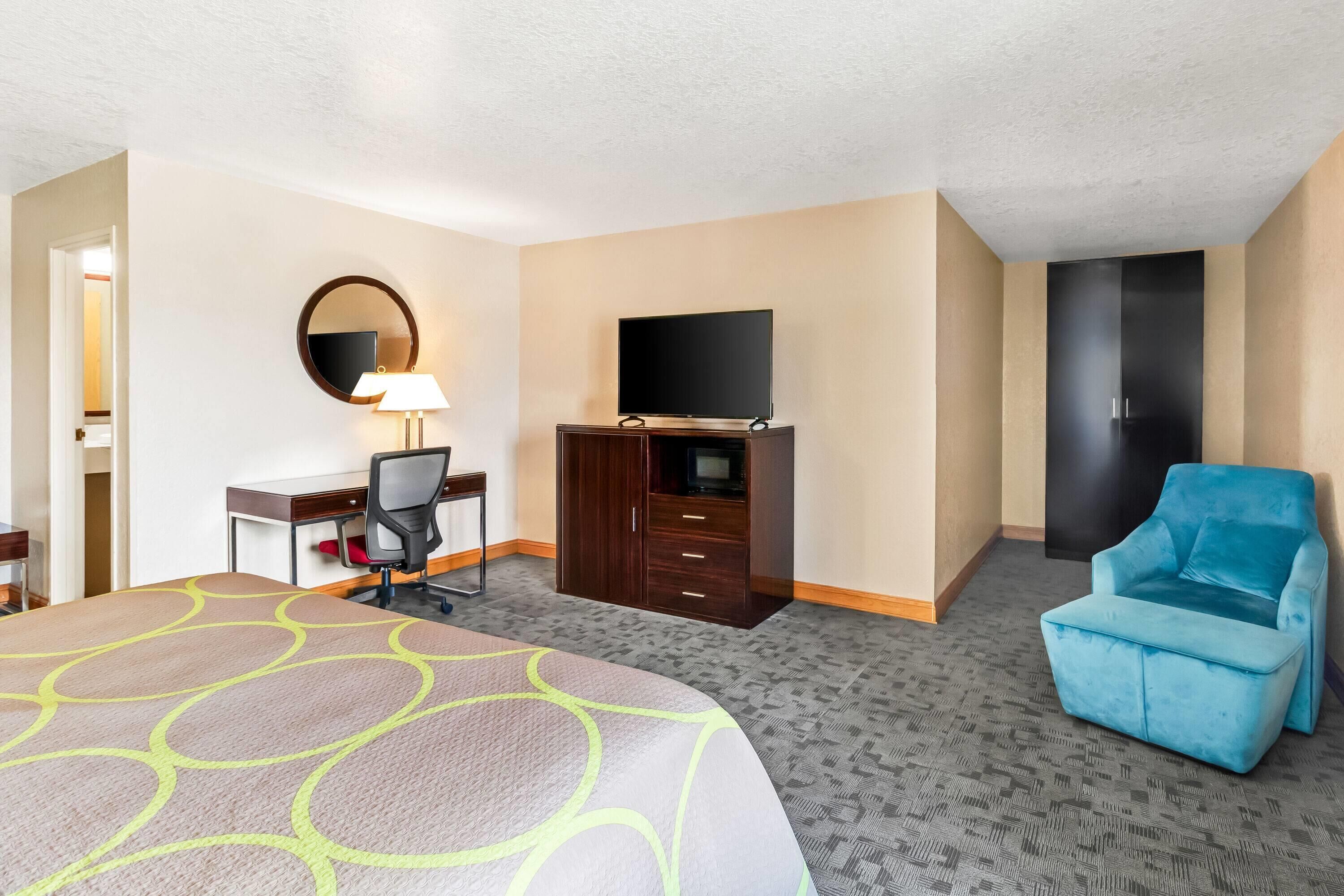Habitación de hotel con cama, escritorio, silla, televisor, armario y puerta.