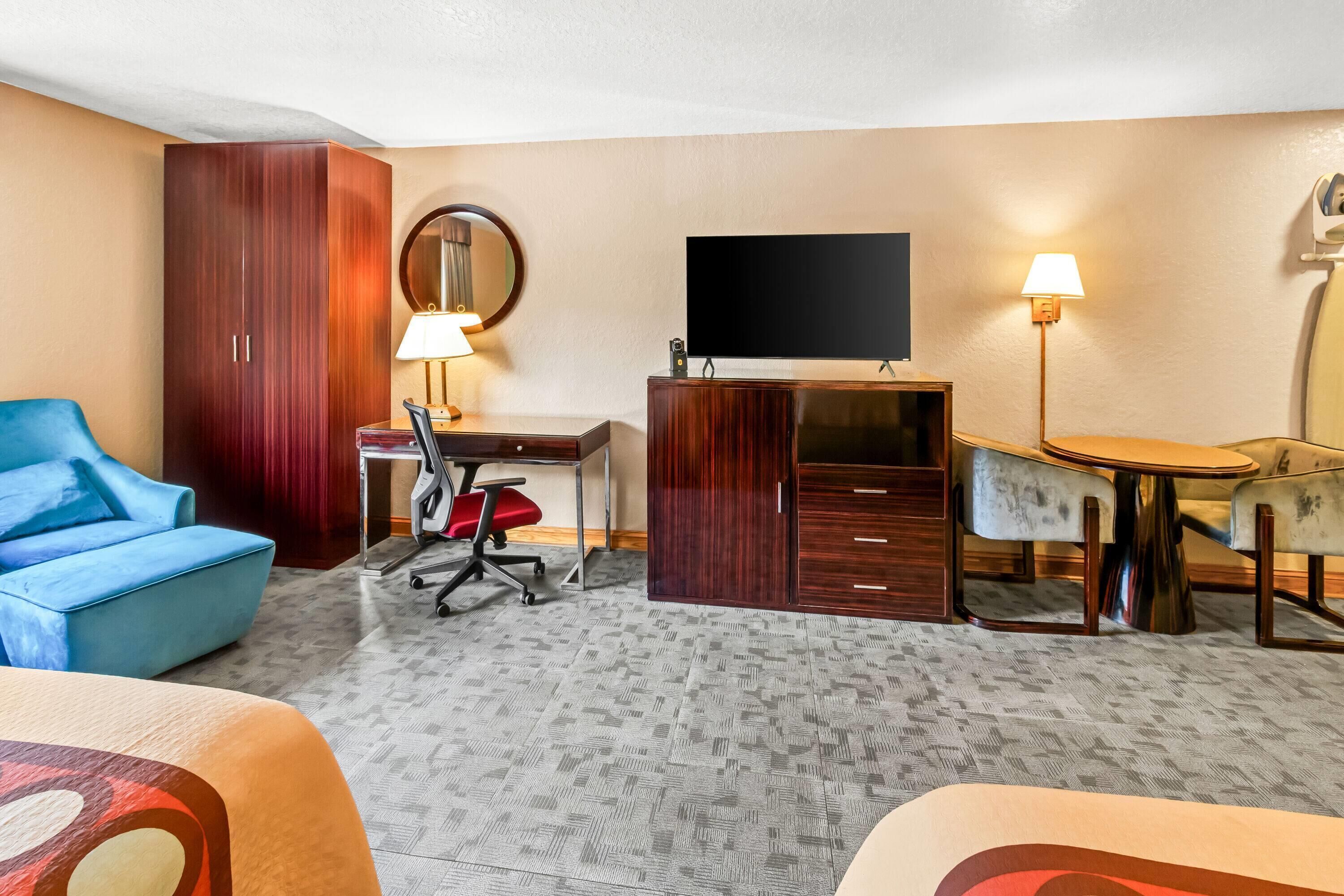 Une chambre d’hôtel avec un canapé bleu, un bureau avec une chaise, une télévision, une armoire et une lampe.