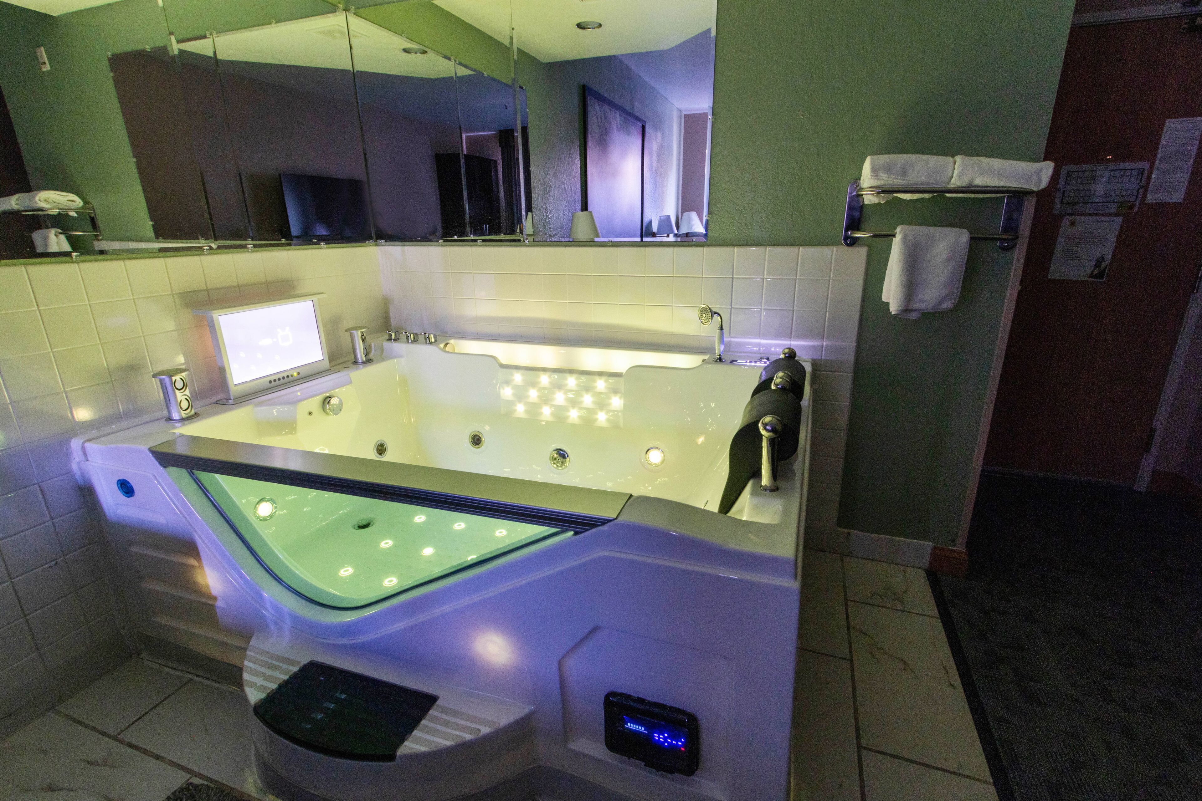 Een moderne badkamer met een groot bad, een digitaal bedieningspaneel en een spiegel boven de wastafel.