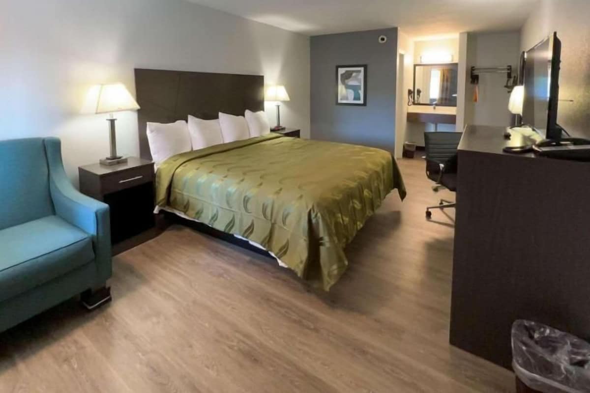 A hotel room with a bed, a desk, a chair, and a small sofa.