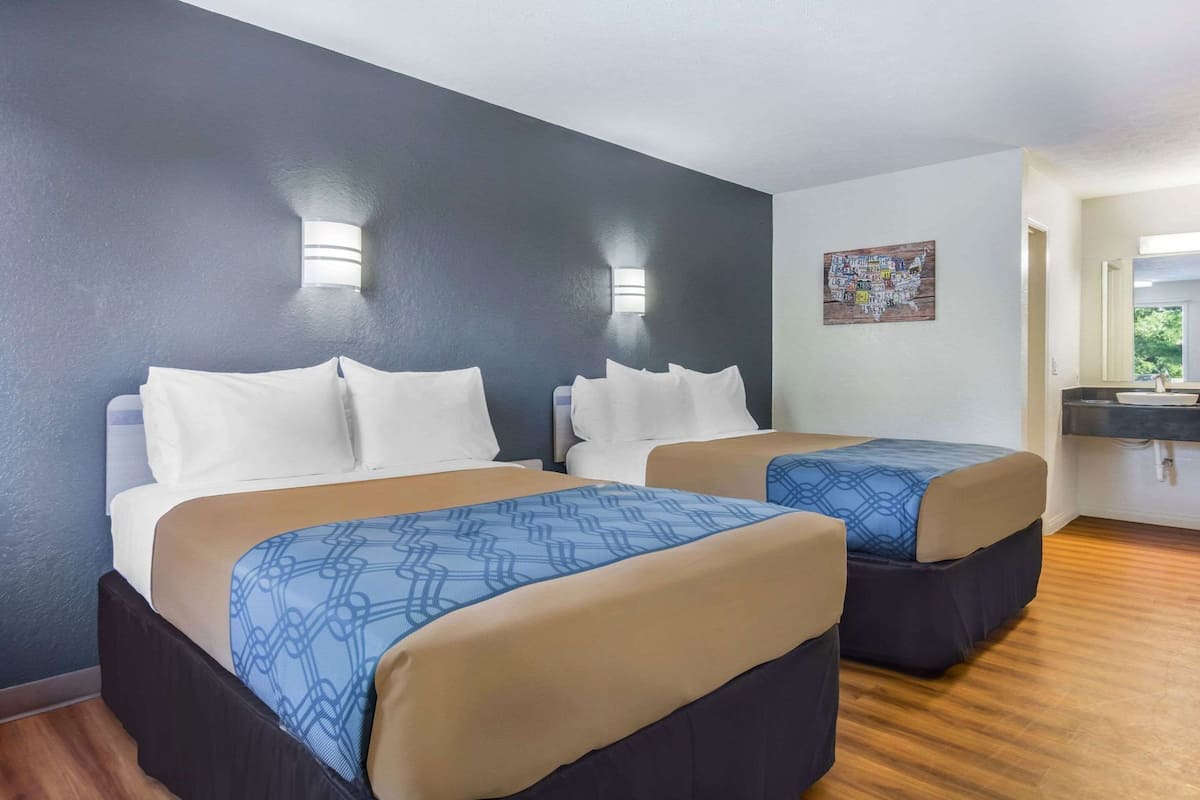 A hotel room with two beds, a window, a sink, and a wall with a clock.