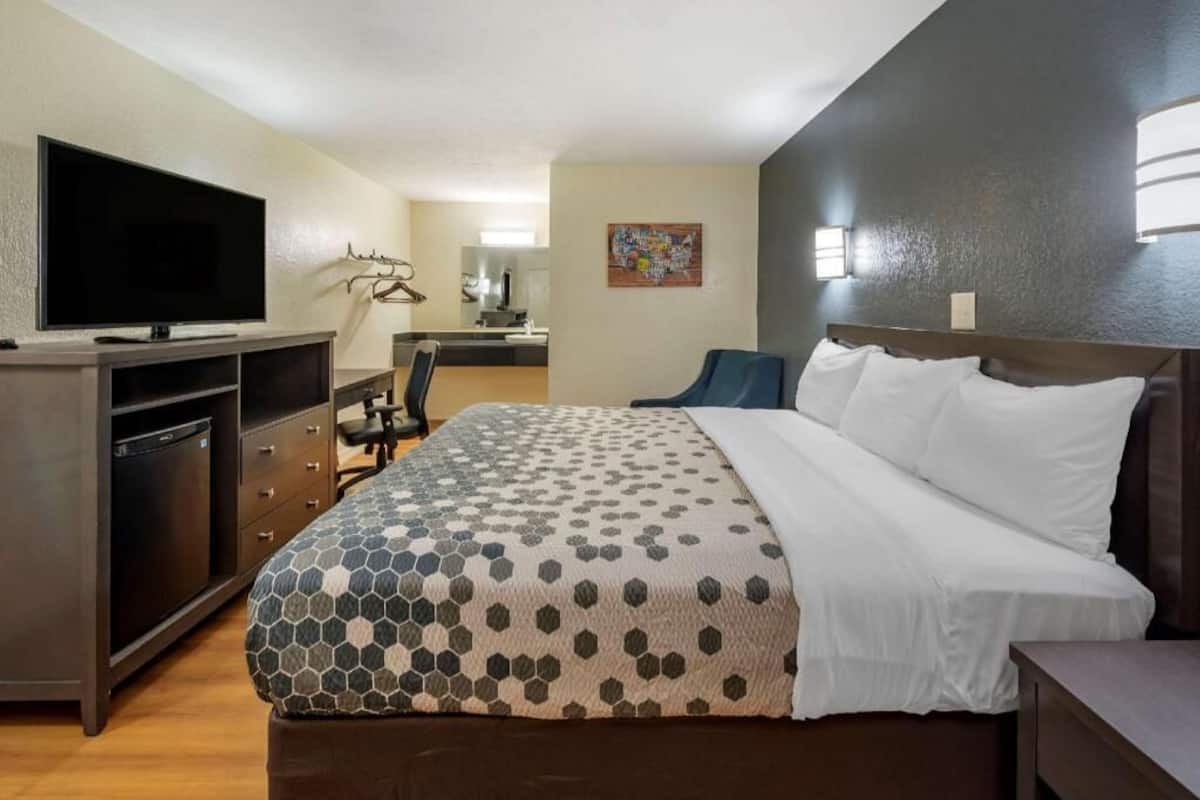 A hotel room with a bed, a desk with a chair, a television, and a bathroom visible in the background.