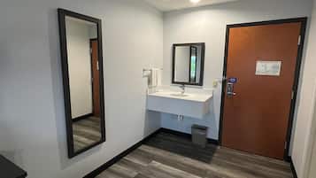Une salle de bain d’hôtel avec un sol en bois, un lavabo blanc, un miroir et une porte avec une pancarte.