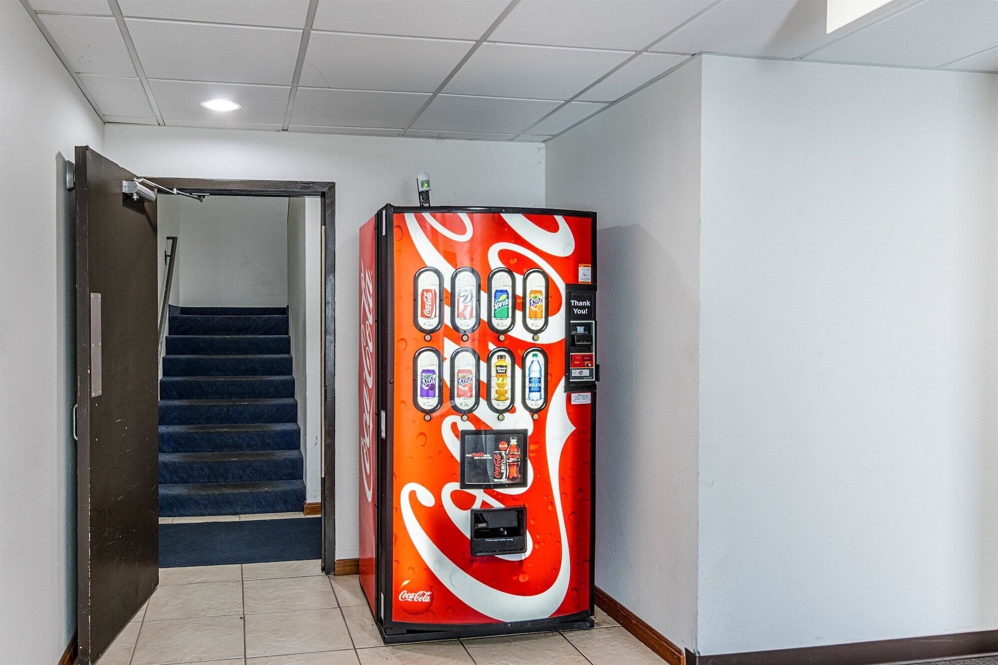 A Coca-Cola vending machine in a hallway with a staircase.
