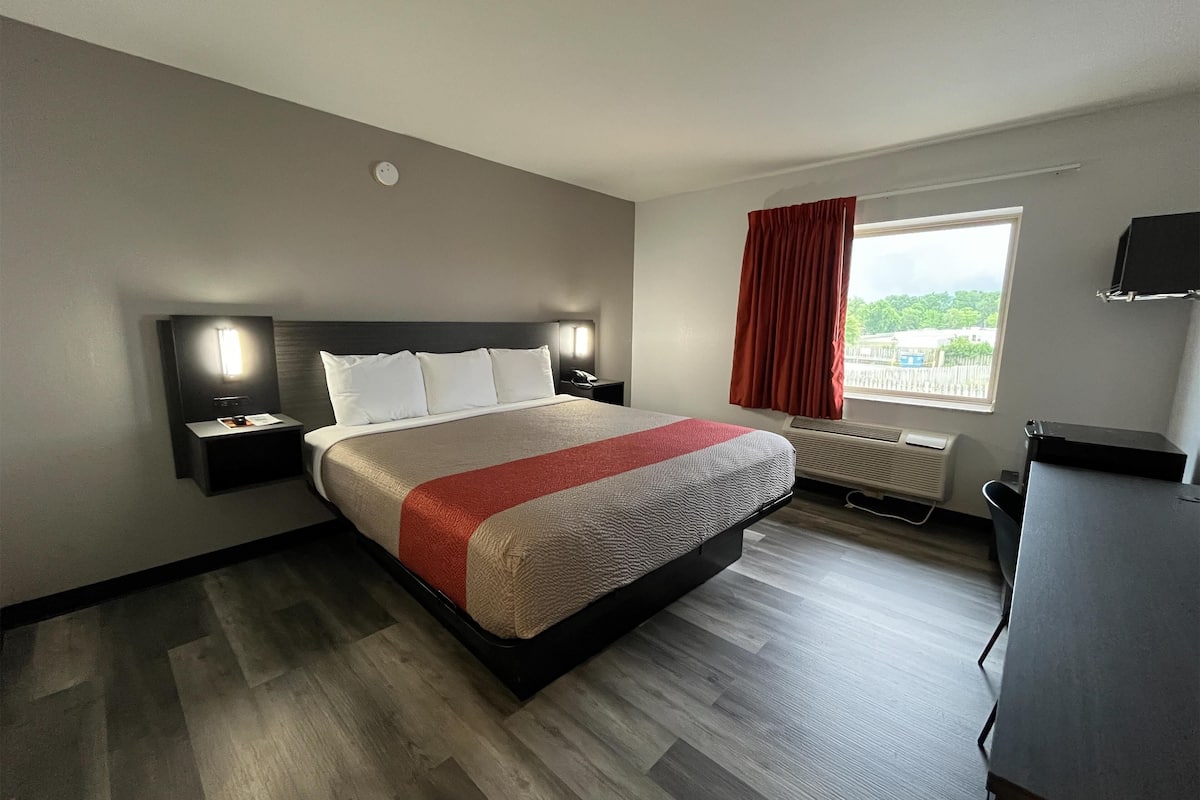 A hotel room with a large bed, bedside tables, a desk, a window with a view, and a wall-mounted TV.