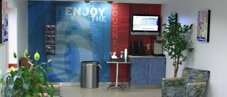 A reception area with a blue wall, a television, a trash bin, a small table with a plant, and a patterned chair.
