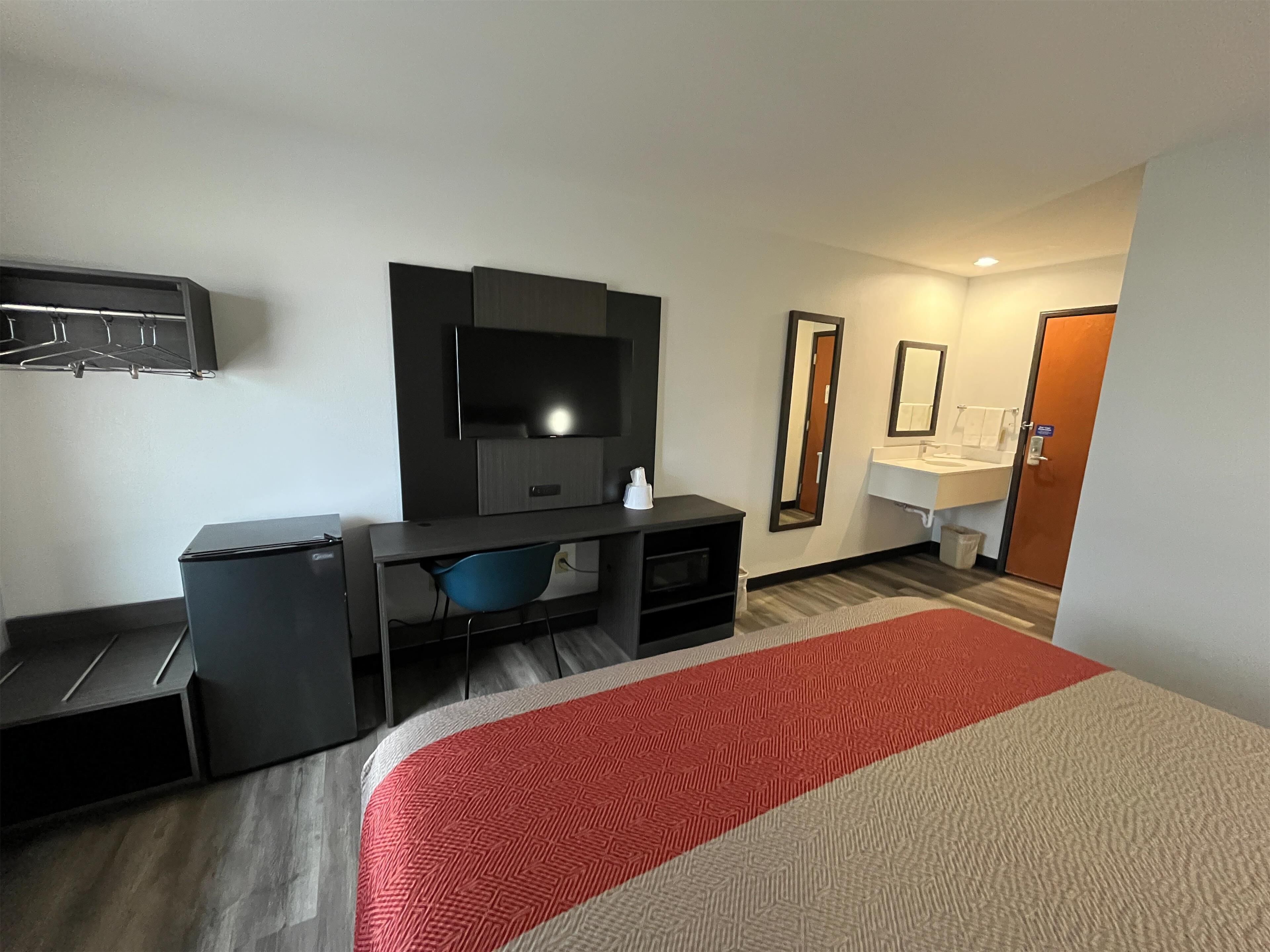 Una habitación de hotel con cama, escritorio, televisión, espejo y baño.