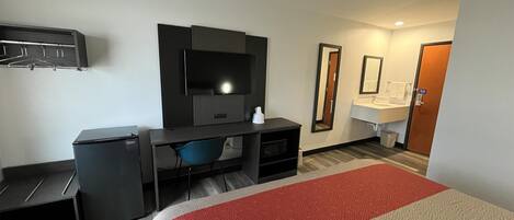 Una habitación de hotel con cama, escritorio, televisión, espejo y baño.