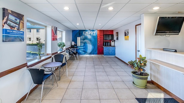 A hotel reception area with a tiled floor, a reception desk, a television, and a large wall mural. - Motel 6 Urbana, IL (Urbana)