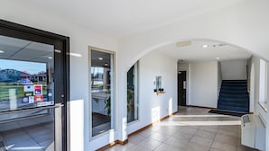 A modern hotel lobby with a glass door, a staircase, and a view of the outside. - Motel 6 Urbana, IL (Urbana)