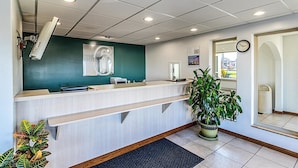 A reception desk with a digital screen, a clock, and a plant. - Motel 6 Urbana, IL (Urbana)