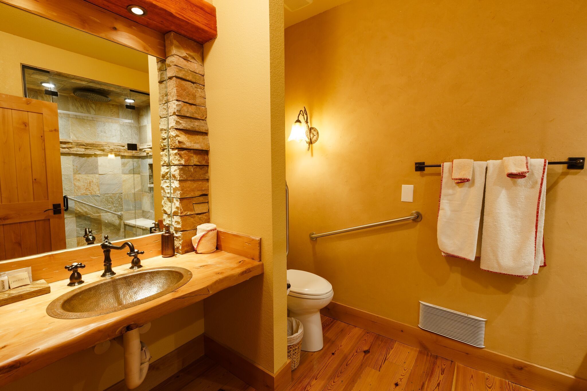 A bathroom with a wooden vanity, a stone accent wall, a white toilet, and a towel rack with towels.