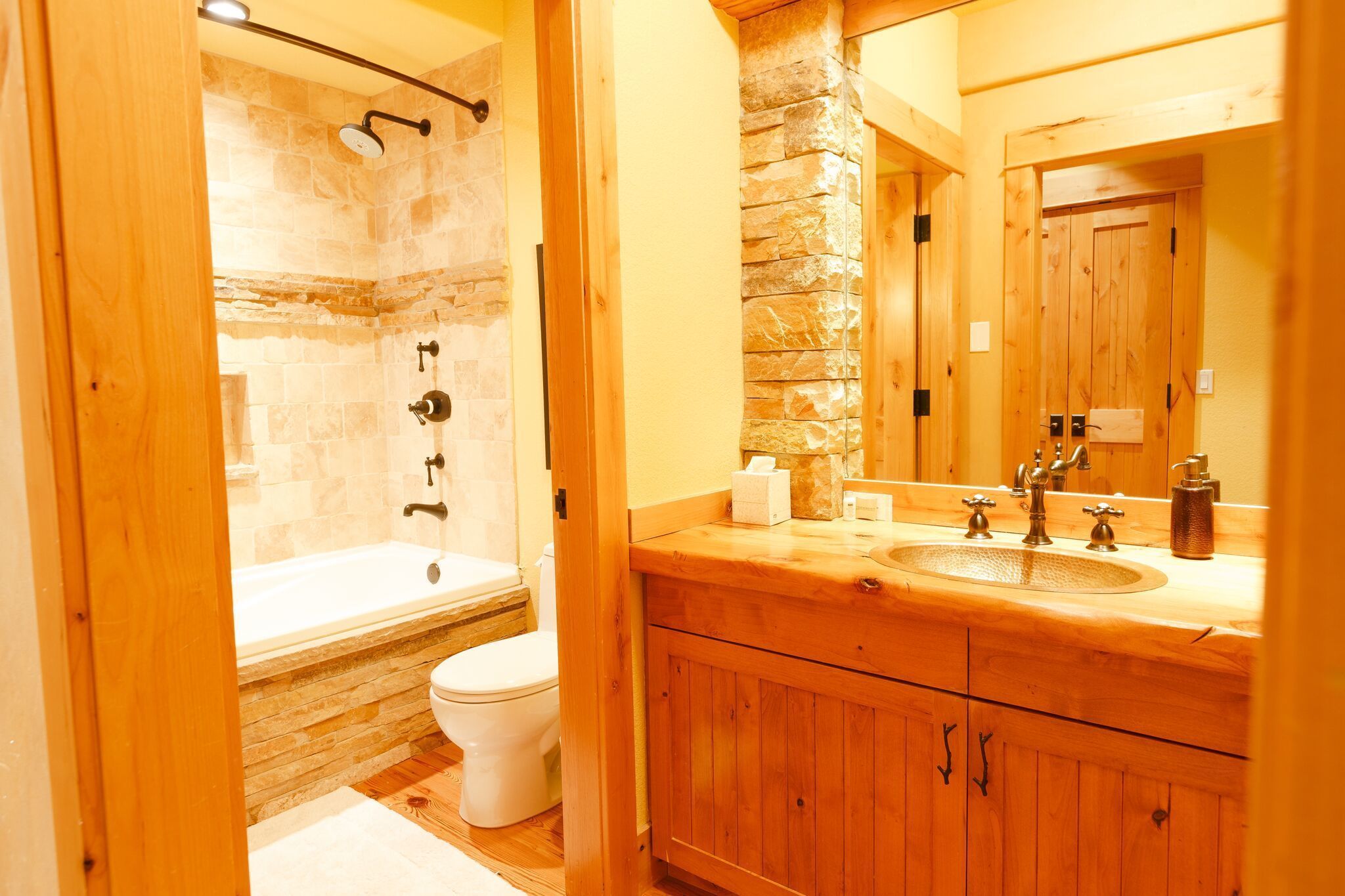 A bathroom with a stone shower, a wooden vanity, and a large mirror.