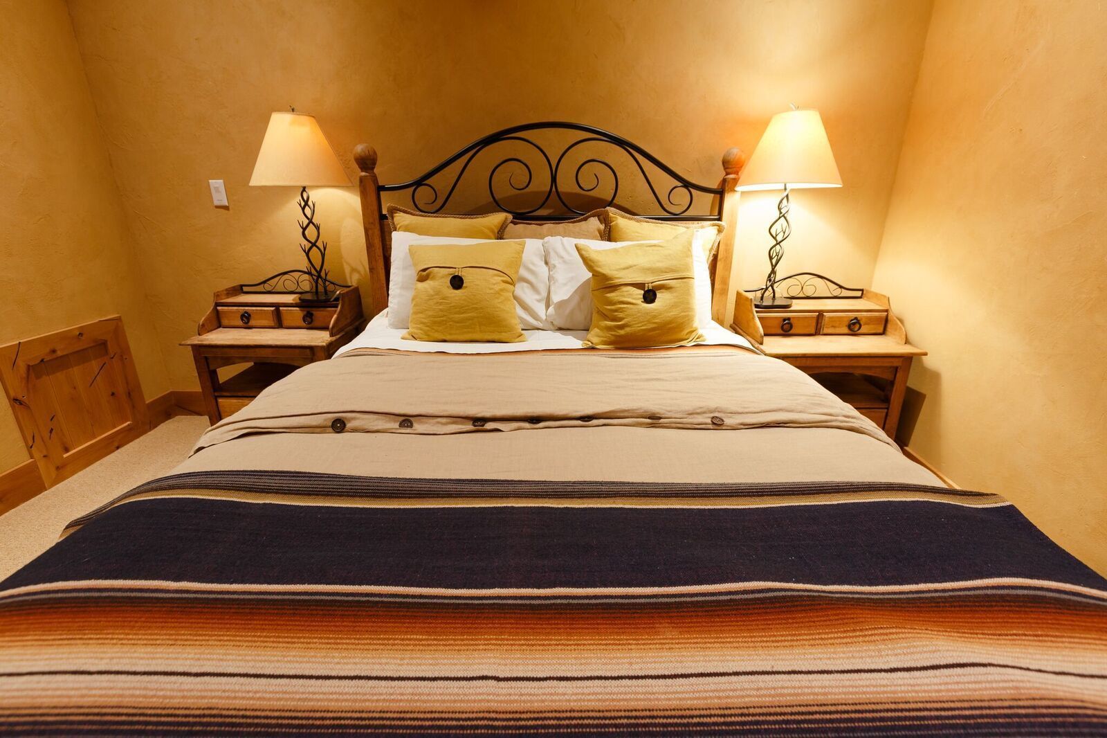 Una cama bien hecha con un edredón a rayas, dos lámparas de noche y dos mesitas de noche de madera con lámparas.