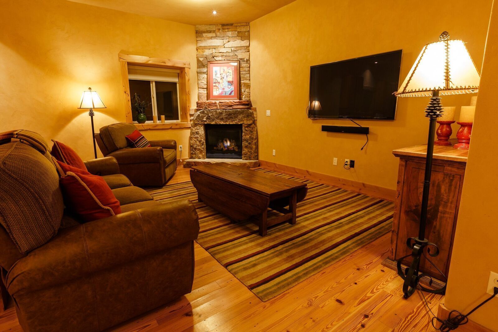 A living room with a fireplace, leather sofa, wooden coffee table, and a flat-screen TV.