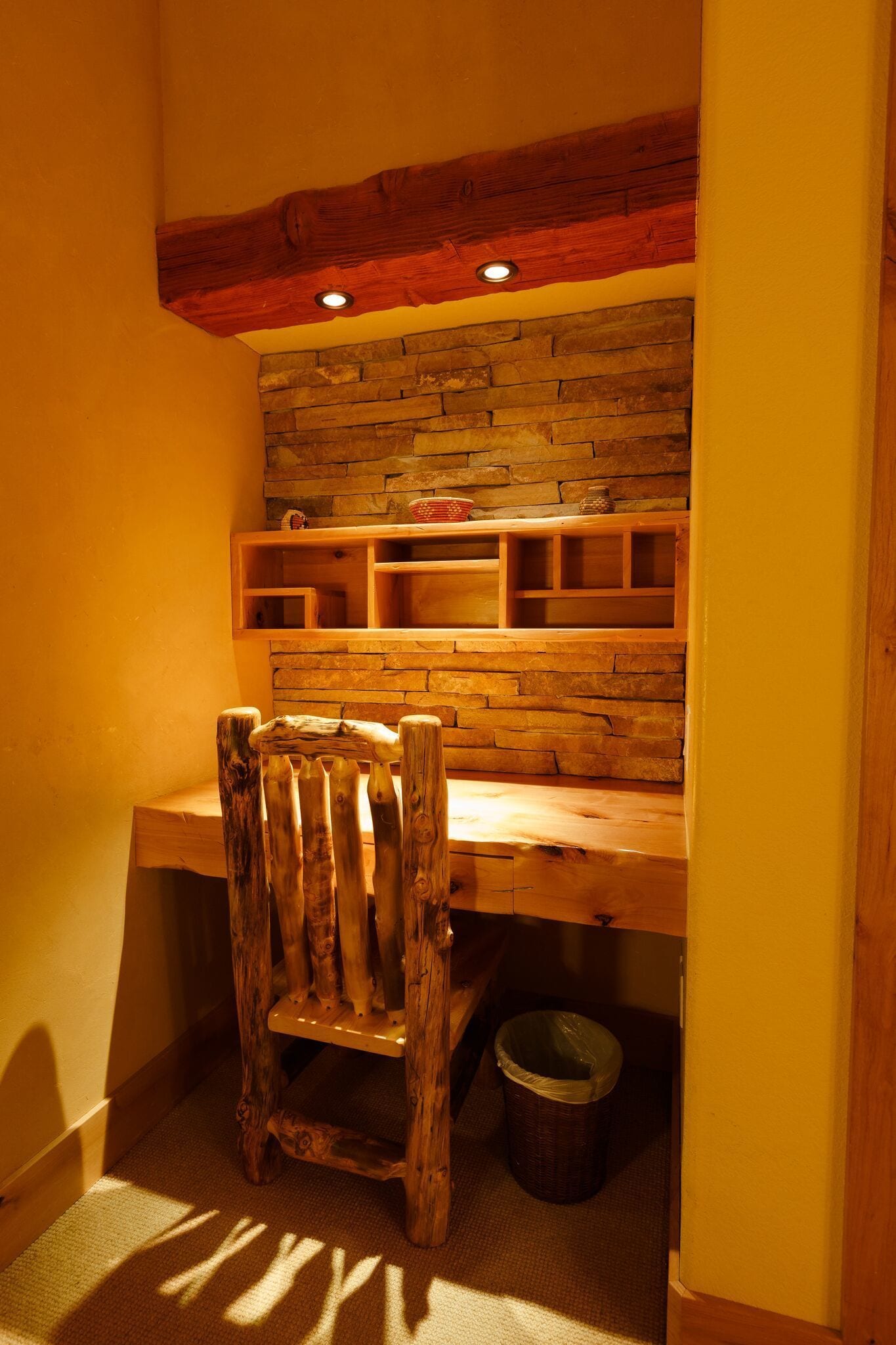 A rustic wooden desk with built-in shelves, a wooden chair, and a stone wall backdrop.