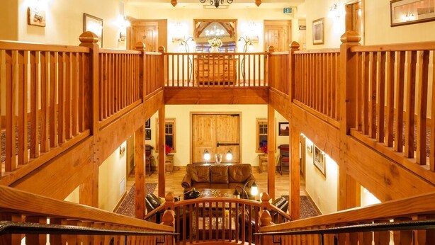 A wooden staircase with a chandelier, leading to a dining area with a high ceiling and wooden beams. - Niwot Inn & Spa (Longmont)