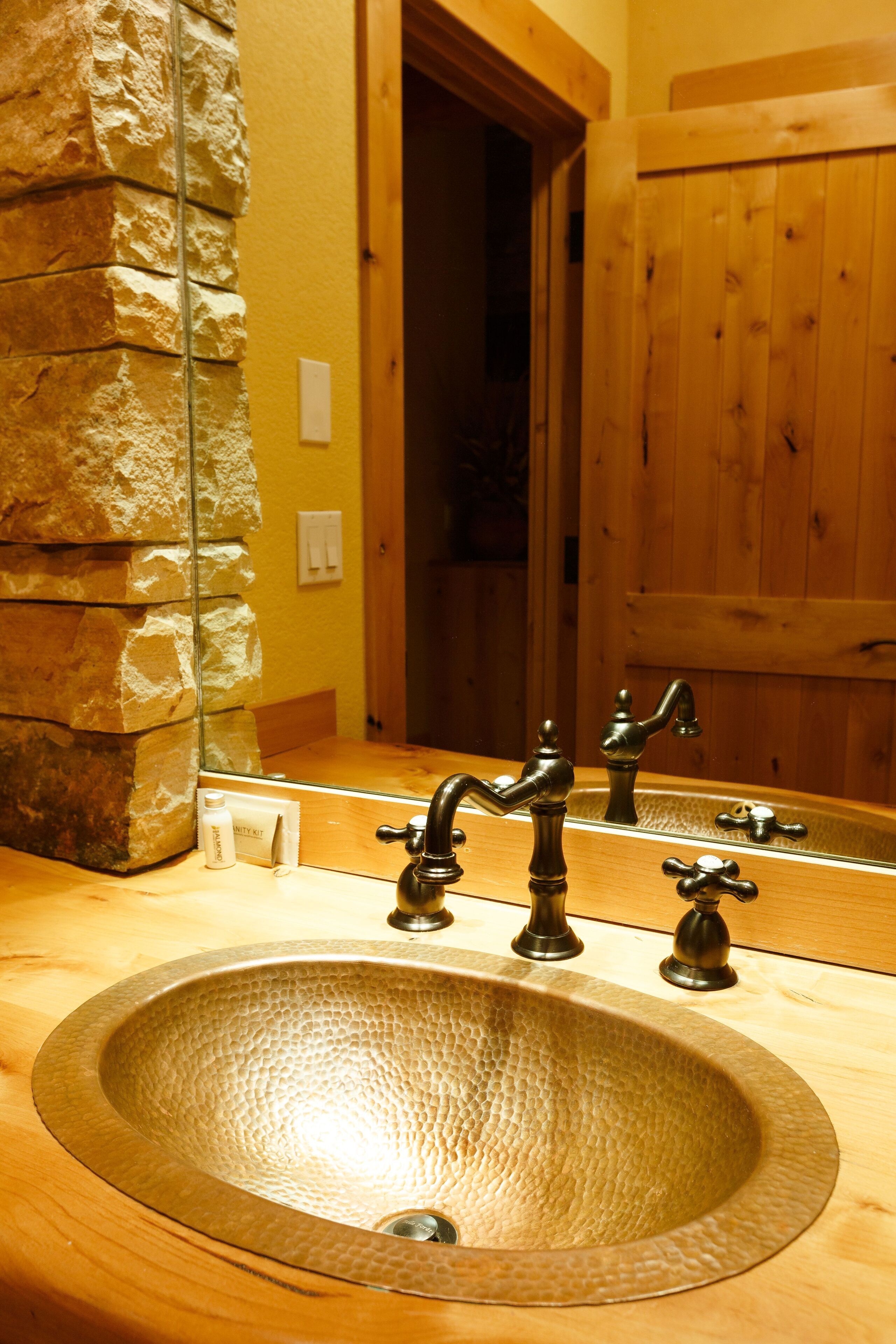 Ein Badezimmer mit Steinwand, Holztür und Waschbecken mit zwei Wasserhähnen.
