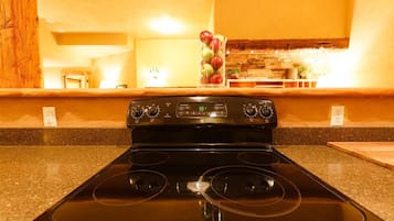 A kitchen with a black stove, granite countertops, and a stone backsplash.