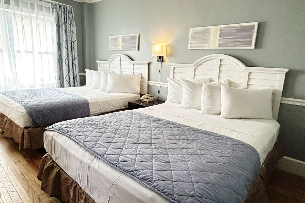 Een hotelkamer met twee bedden, een nachtkastje, een lamp en kunst aan de muur.