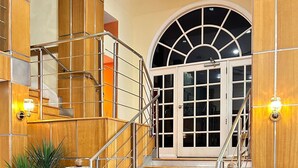 Una escalera con peldaños de madera y barandillas metálicas que conduce a una puerta con paneles de vidrio.