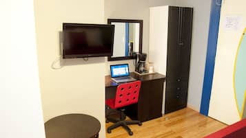 A small room with a desk, a chair, a laptop, a coffee maker, a TV, and a wardrobe.