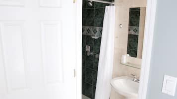 Un baño con puerta blanca, ducha con puerta de cristal, lavabo y espejo.