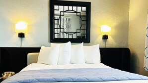 Habitación de hotel con cama, almohadas blancas, cabecera, dos lámparas fijadas a la pared y un teléfono sobre la mesita de noche.