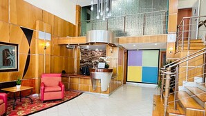 Un vestíbulo de hotel con mostrador de recepción, una escalera y una zona de estar con una silla roja.
