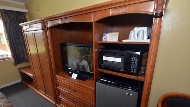A compact room with a wooden entertainment unit, a television, a microwave, and a refrigerator. - Gateway Inn (Red Bluff)