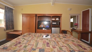 A bedroom with a bed, a television, a microwave, and a small table with a vase. - Gateway Inn (Red Bluff)