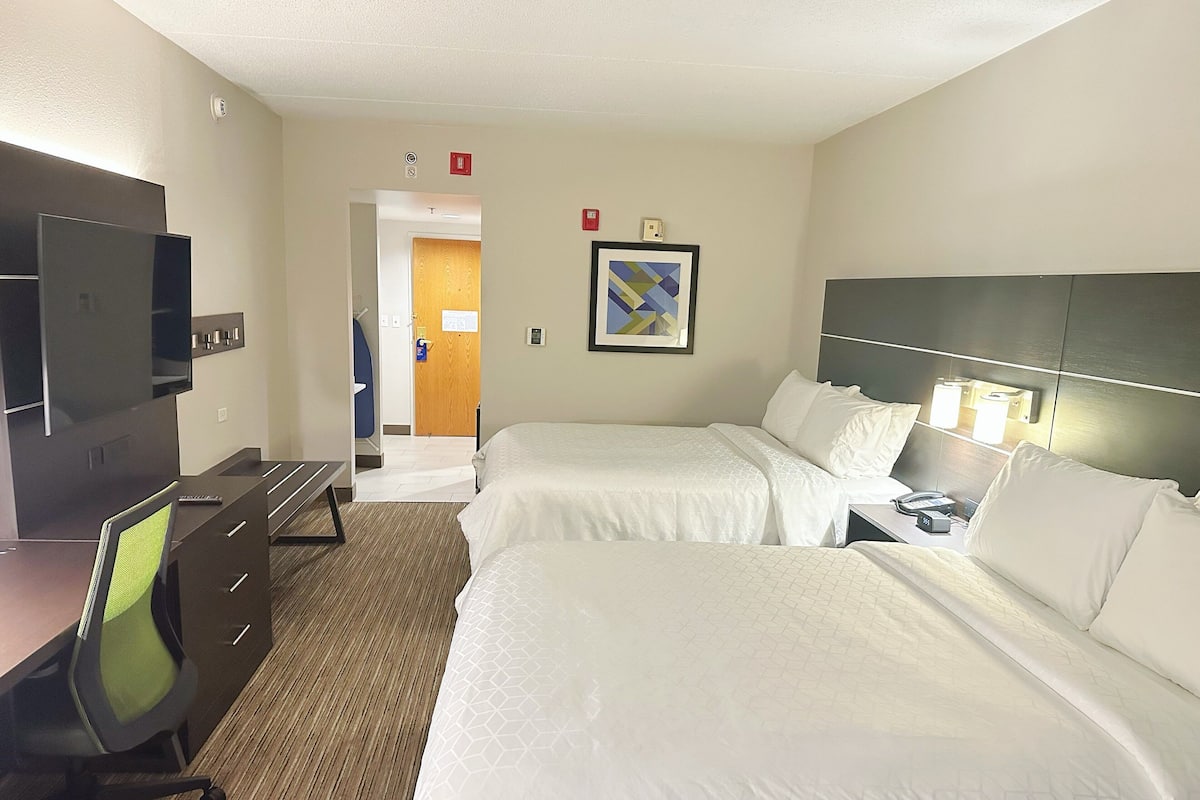 A hotel room with two beds, a desk, a chair, a TV, and a door leading to a bathroom.
