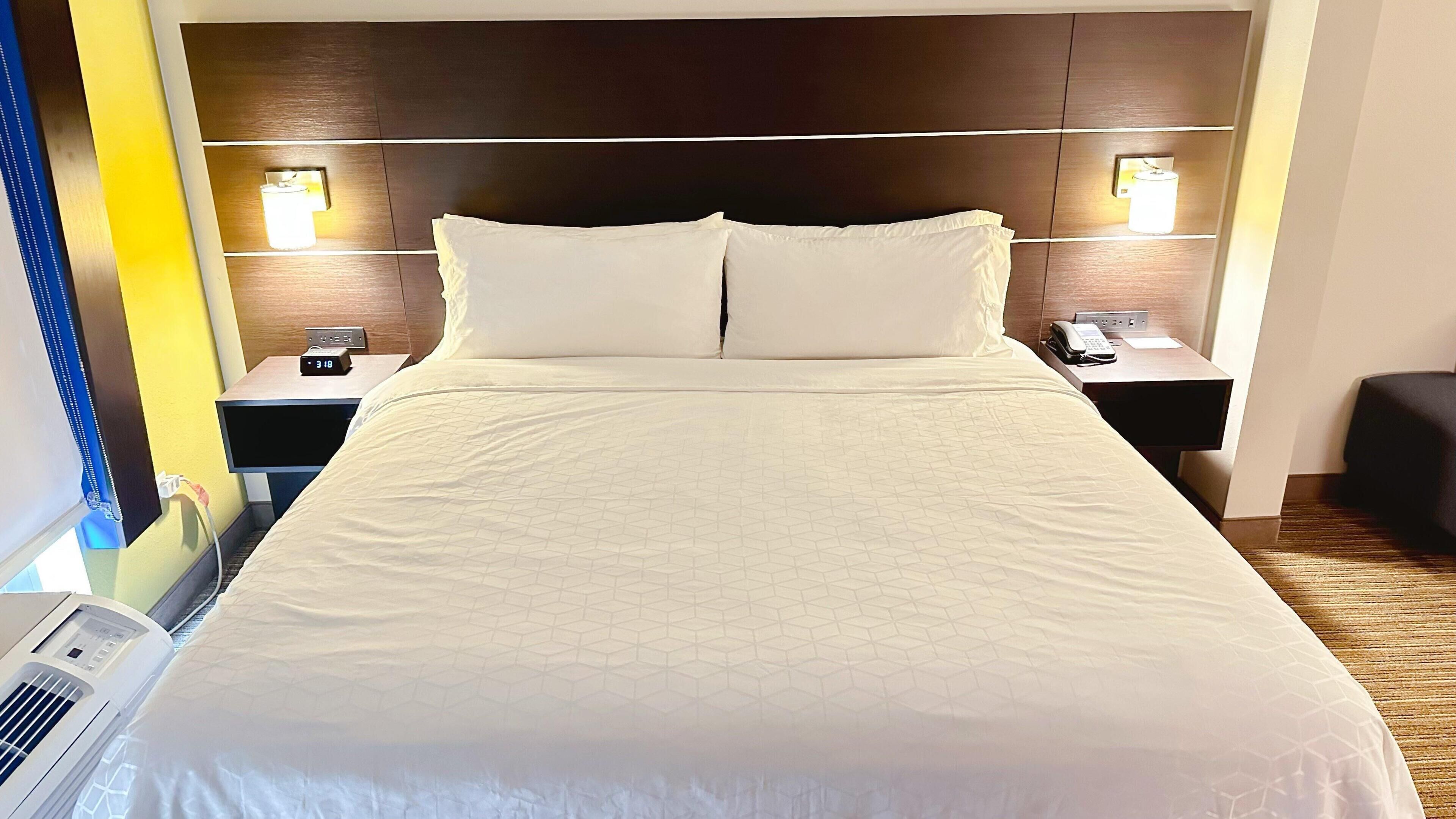 Hotellihuone, jossa on suuri sänky, kaksi yöpöytää valaisimineen, seinään asennettu ilmastointilaite ja puhelin yöpöydällä.