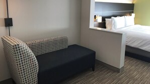 A hotel room with a bed, a nightstand, a lamp, and a sofa.