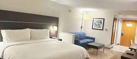 A hotel room with a large bed, a desk, a chair, and a door.