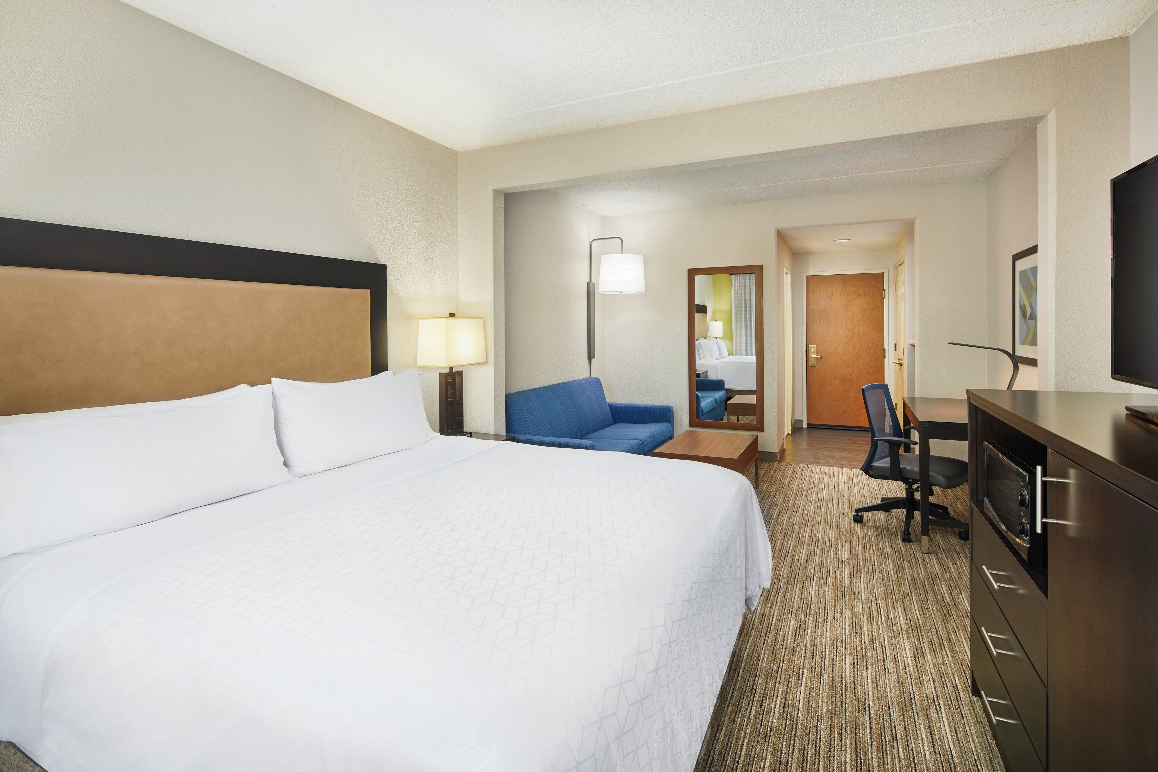 A hotel room with a large bed, a desk, a chair, a television, and a mirror.