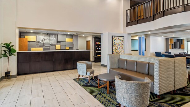 A lobby with a reception desk, seating area, and a staircase. - Holiday Inn Express & Suites Jacksonville SE- Med Ctr Area by IHG (Jacksonville)