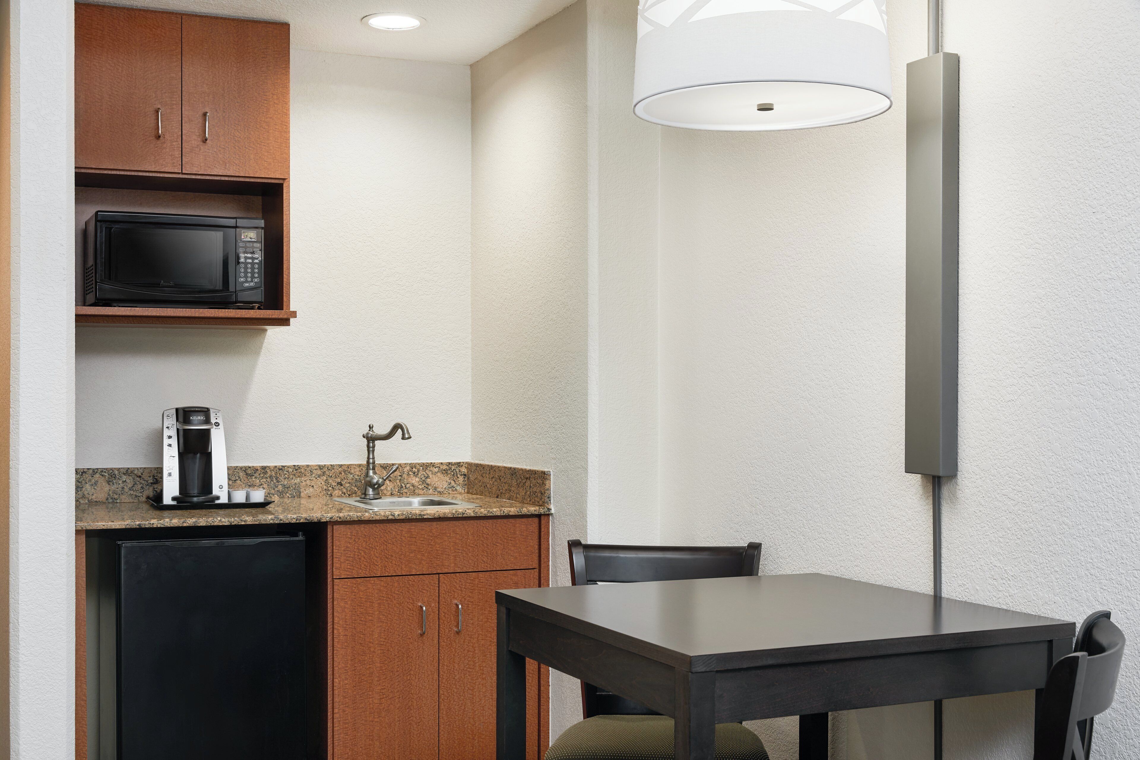 Una kitchenette compacta con microondas, cafetera y lavamanos.