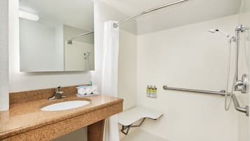 Un baño con lavamanos de encimera de granito, un espejo, ducha con cabezal de ducha manual y un perchero para toallas.