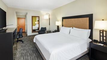 Habitación de hotel con una cama grande, un escritorio con televisor, una silla y una lámpara de escritorio.