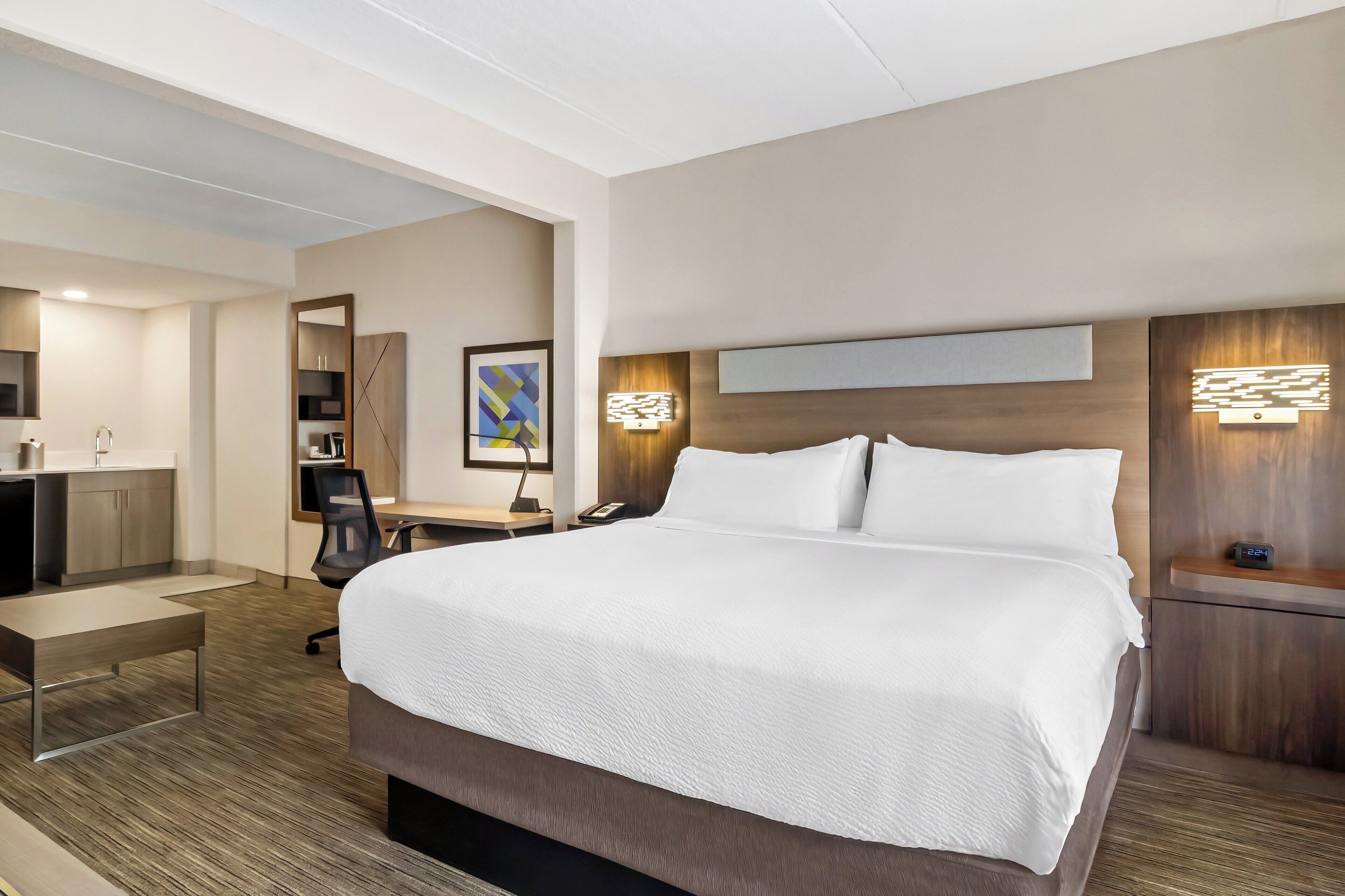 Et moderne hotelværelse med en stor seng, et skrivebord med stol, et lille bord, en skrivebordslampe, en telefon og en vægmonteret lysarmatur.