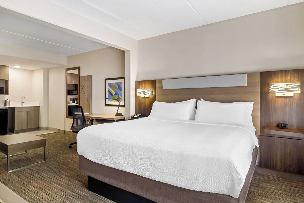 Une chambre d’hôtel moderne, dotée d’un grand lit, d’un bureau avec une chaise, d’une petite table, d’une lampe de bureau, d’un téléphone et d’un luminaire fixé au mur.