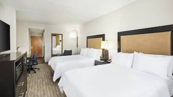 A hotel room with two beds, a desk with a TV, a chair, a lamp, and a door leading to another room.