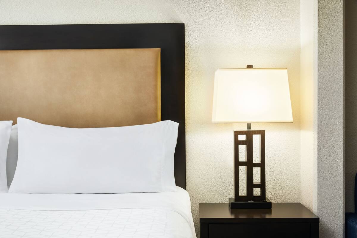 Un lit bien fait, avec du linge de lit blanc et une tête de lit, une table de chevet avec une lampe et un mur à texture.