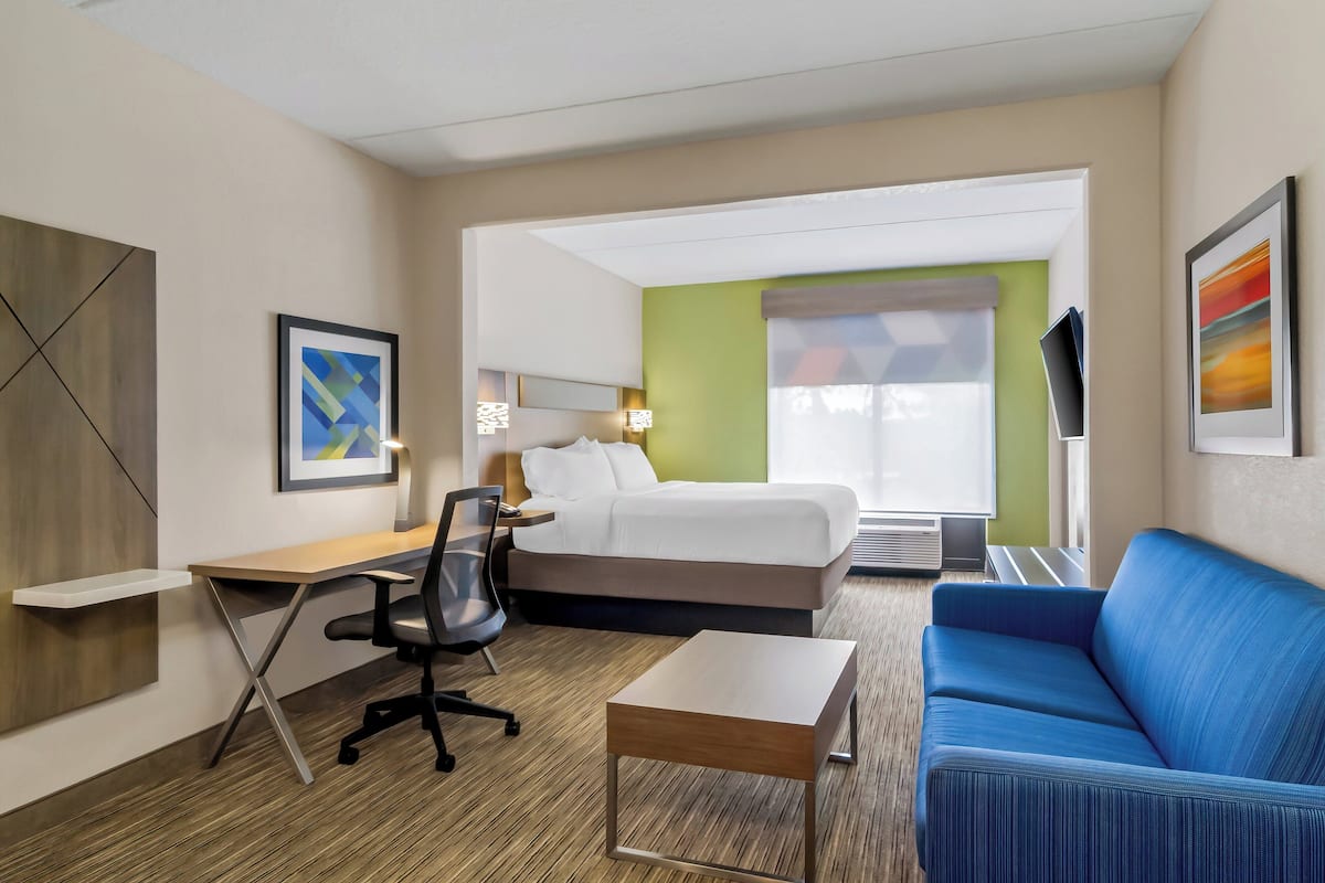 Une chambre d’hôtel avec un lit, un bureau, un canapé bleu et une petite table.