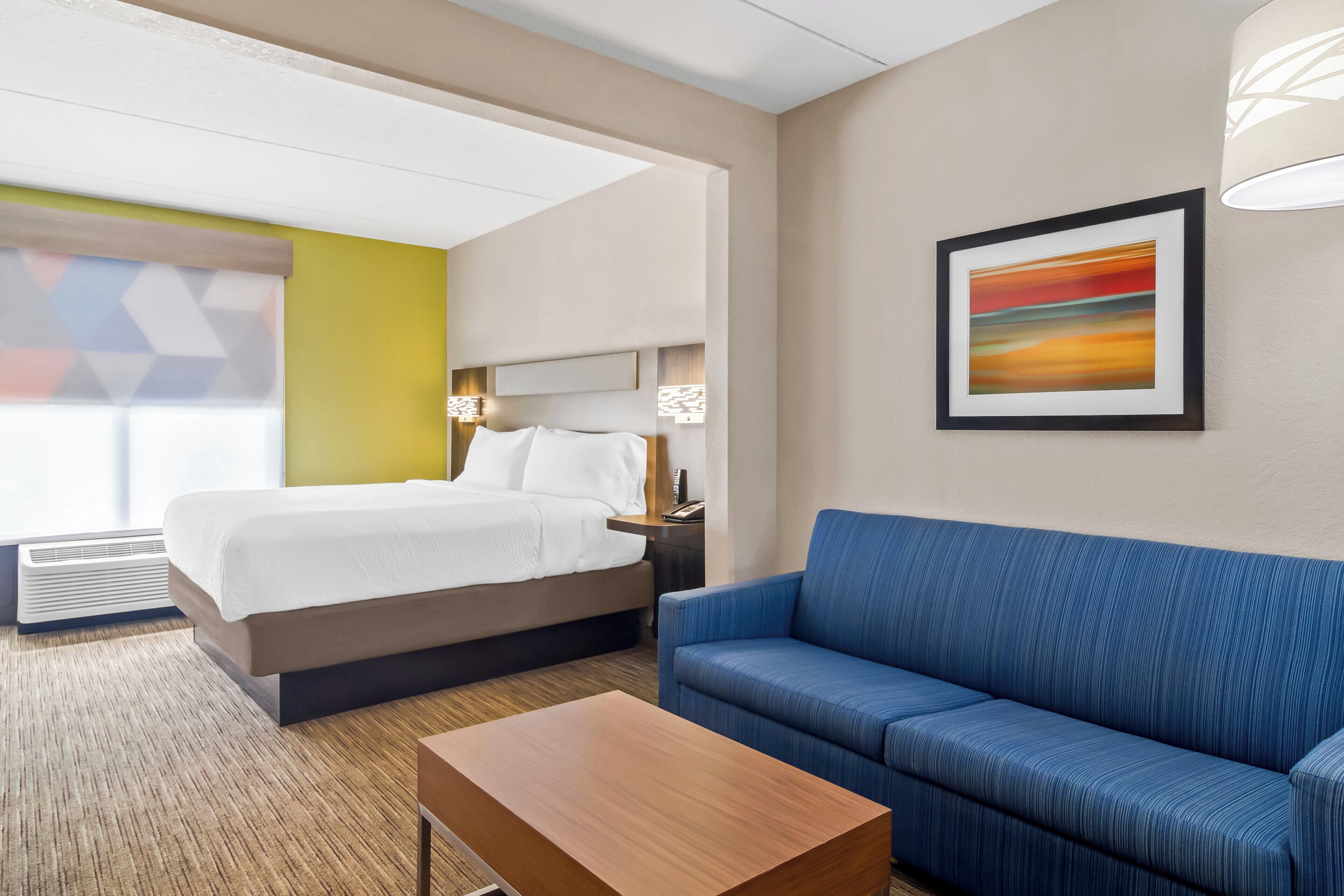 Una habitación de hotel con cama, sofá azul, mesa de madera y un cuadro en la pared.