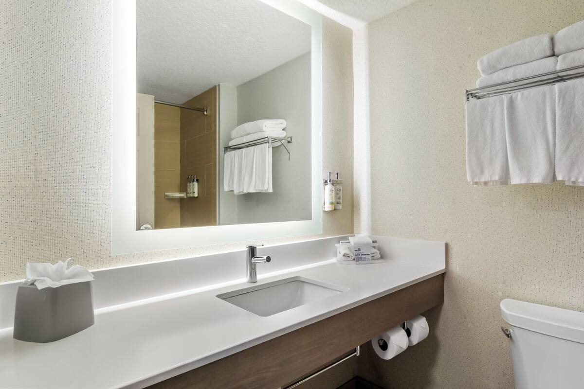 Une salle de bain moderne avec un grand miroir, un lavabo blanc et un porte-serviettes.