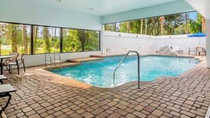 An indoor swimming pool with clear views of trees outside, a tiled floor, and a covered seating area. - Holiday Inn Express & Suites Jacksonville SE- Med Ctr Area by IHG (Jacksonville)